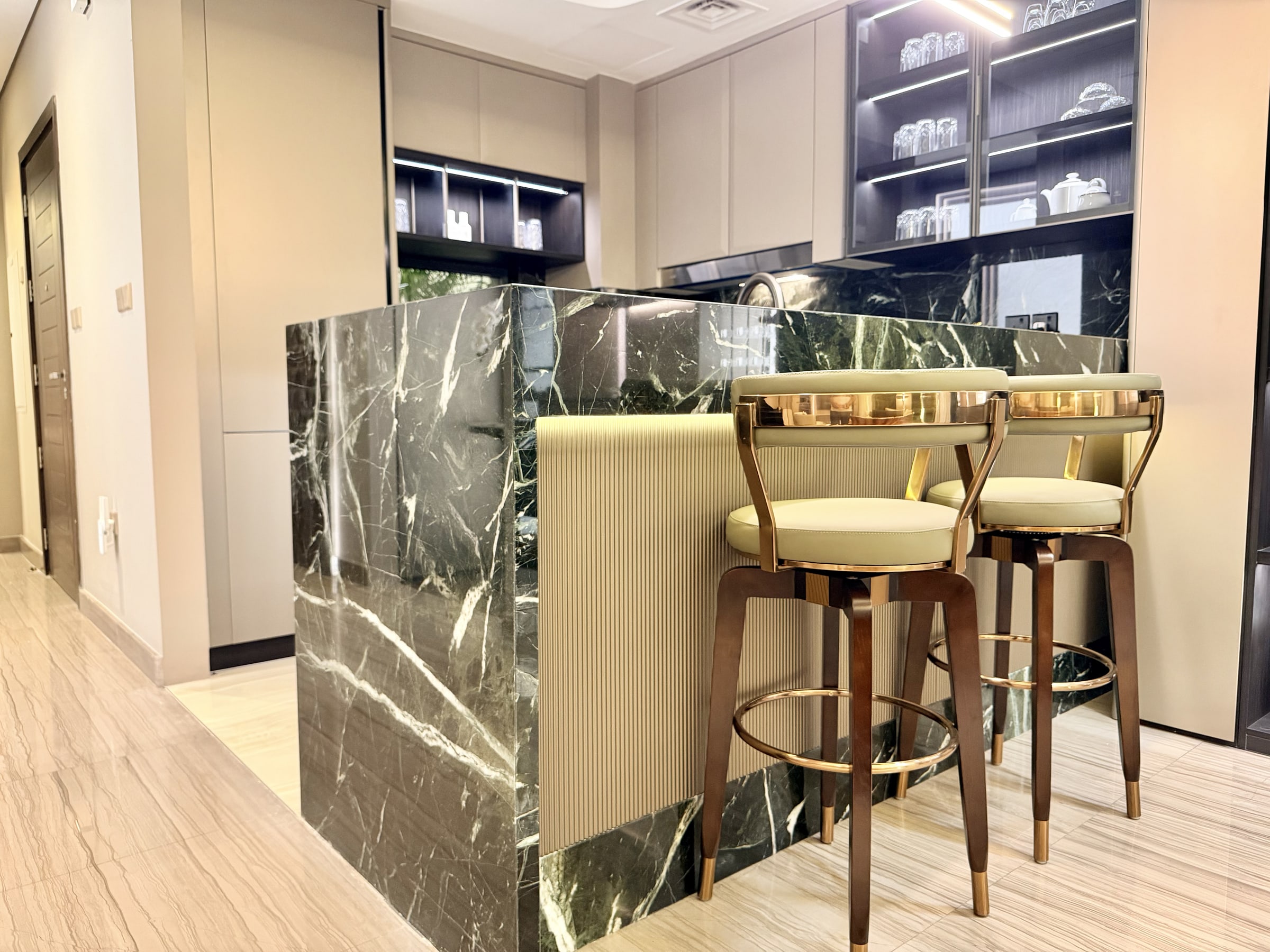 Modern kitchen with a dark green marble island, gold-accented bar stools, integrated lighting and fluted panelling along the back wall