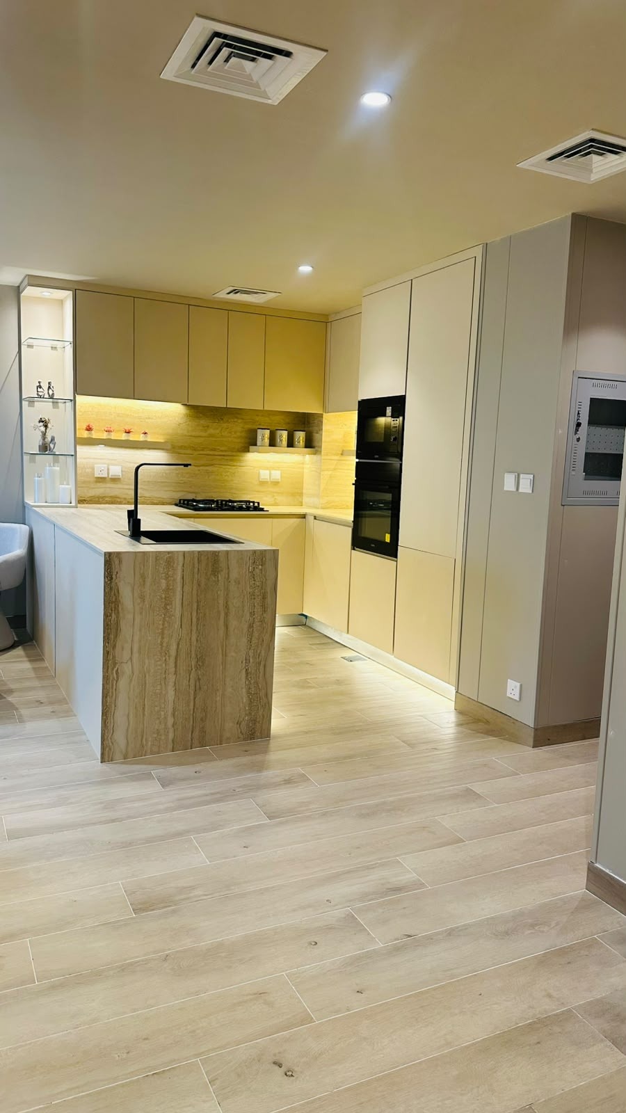 Beige cabinetry with a stone clad island, an integrated black sink and faucet, and under cabinet lighting