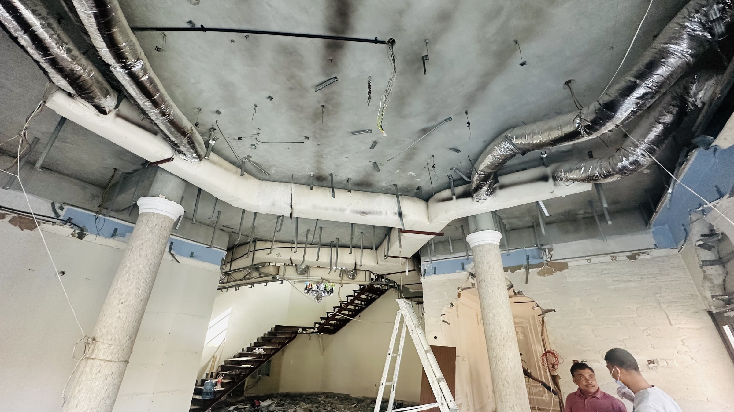 Interior under renovation in Dubai with an exposed concrete ceiling, insulated HVAC ductwork, metal ceiling framing and an unfinished staircase