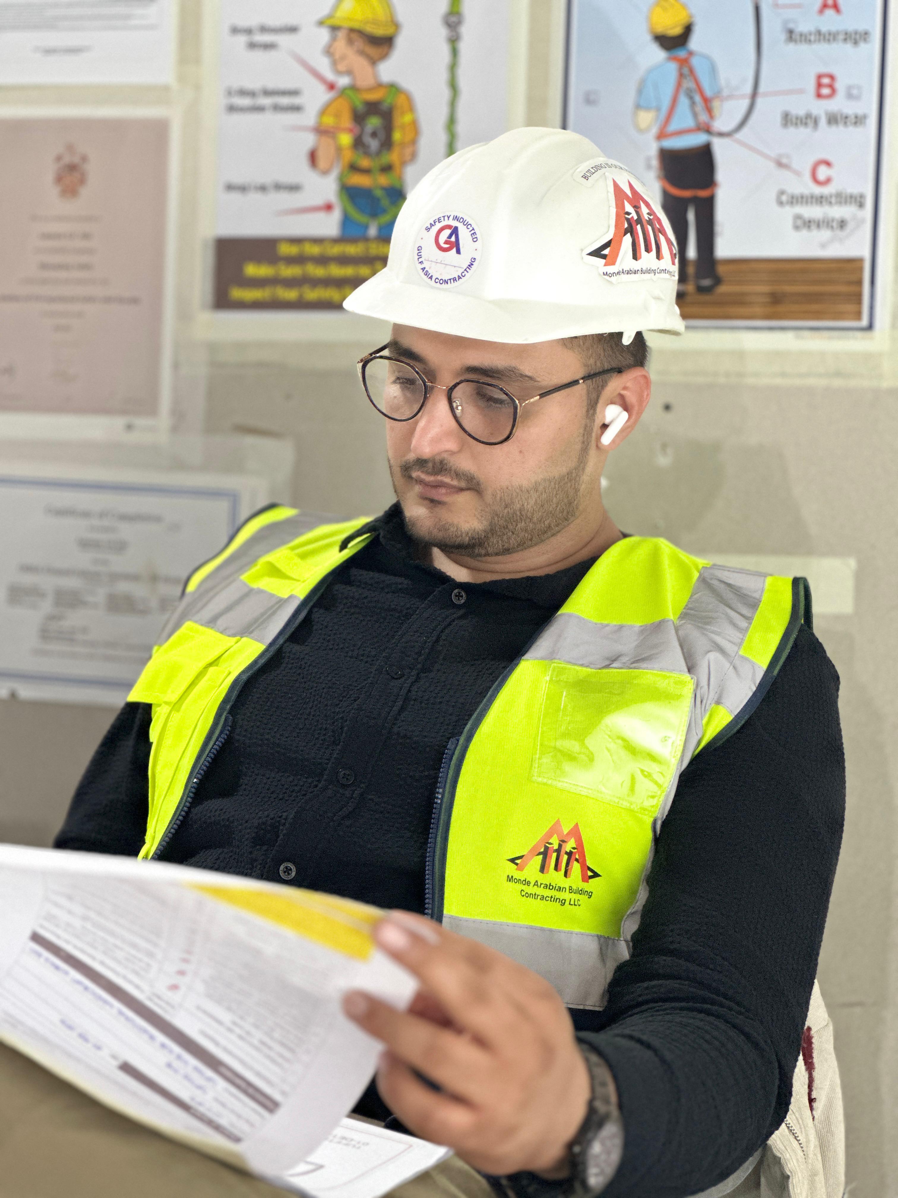 A construction professional, wearing a white hard hat and a high-visibility vest, intently reviewing documents