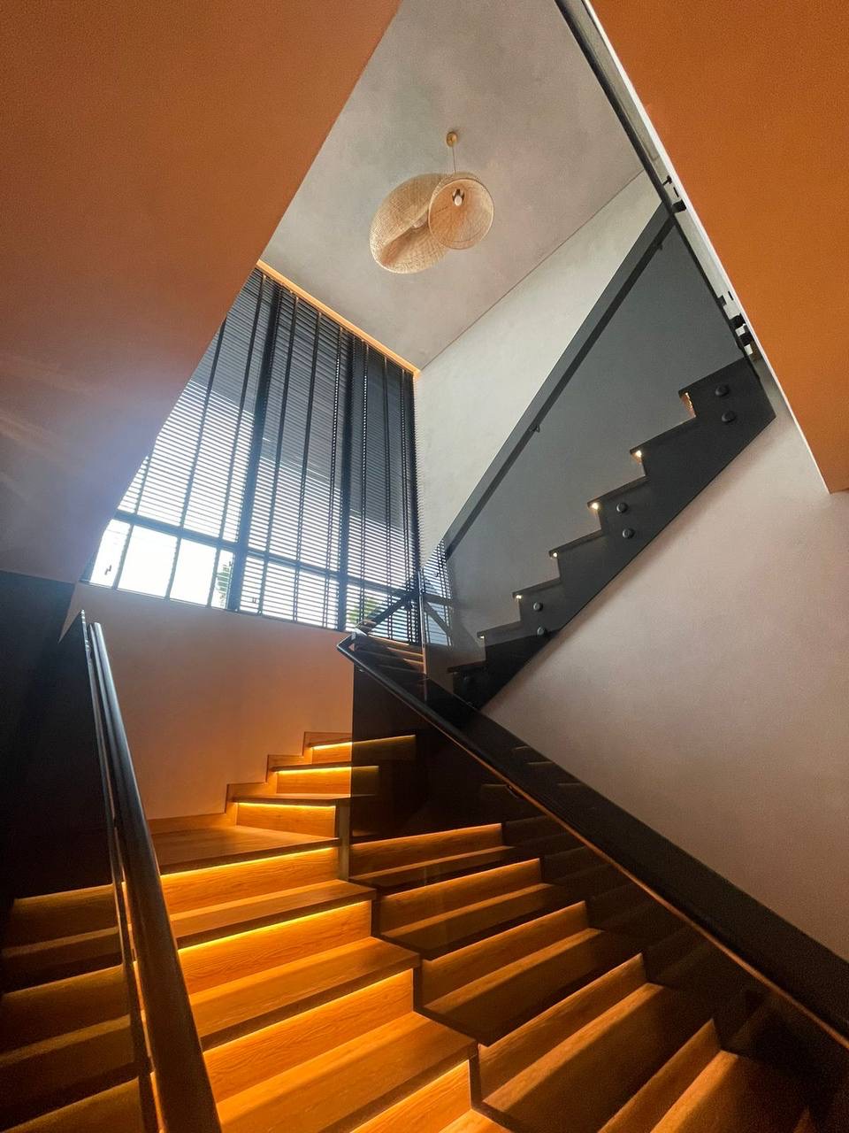 A modern luxury staircase featuring integrated LED lighting, wooden treads, glass railings, and a unique woven pendant light