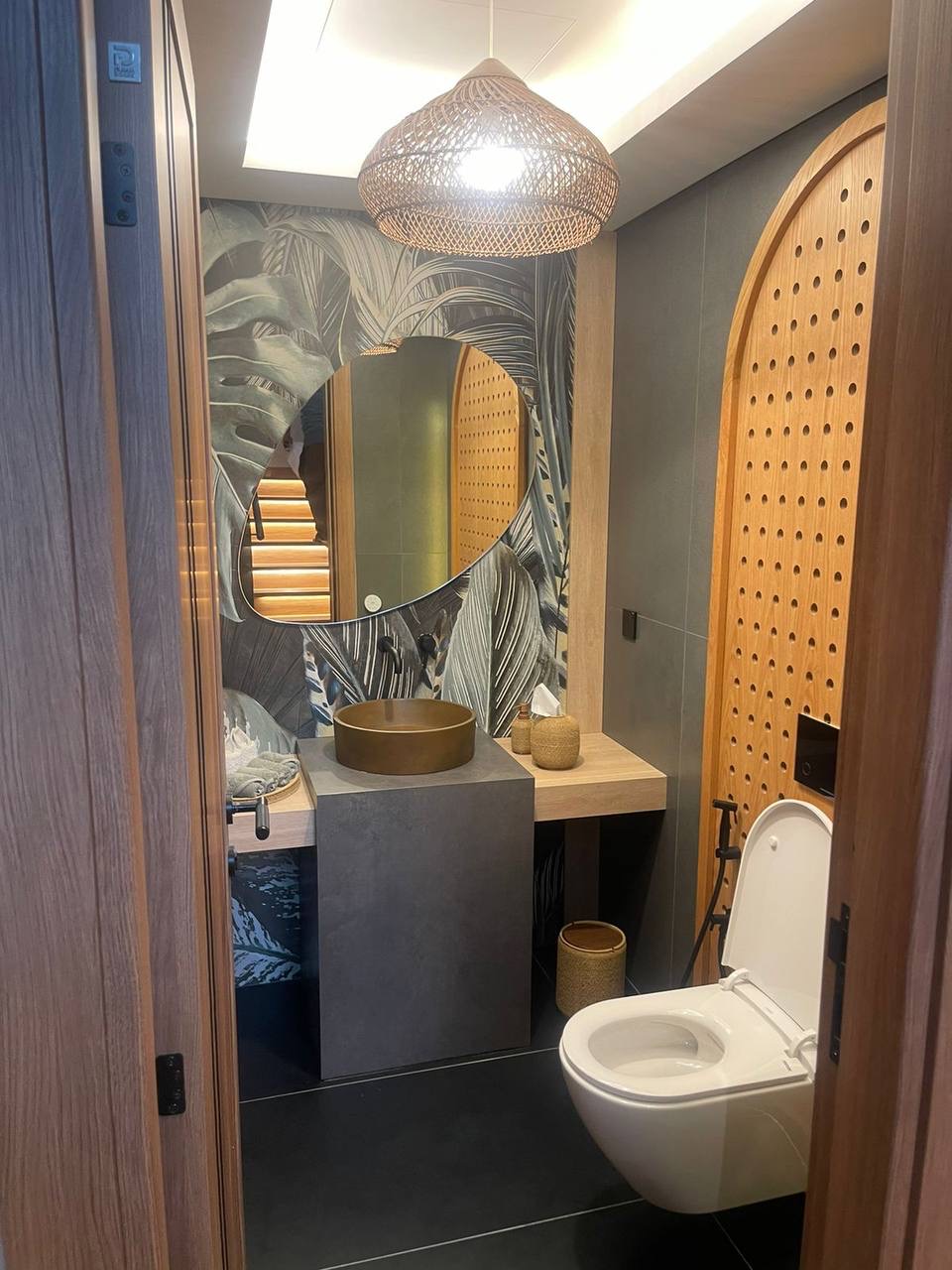 A stylish and modern powder room featuring tropical leaf wallpaper and bronze vessel sink