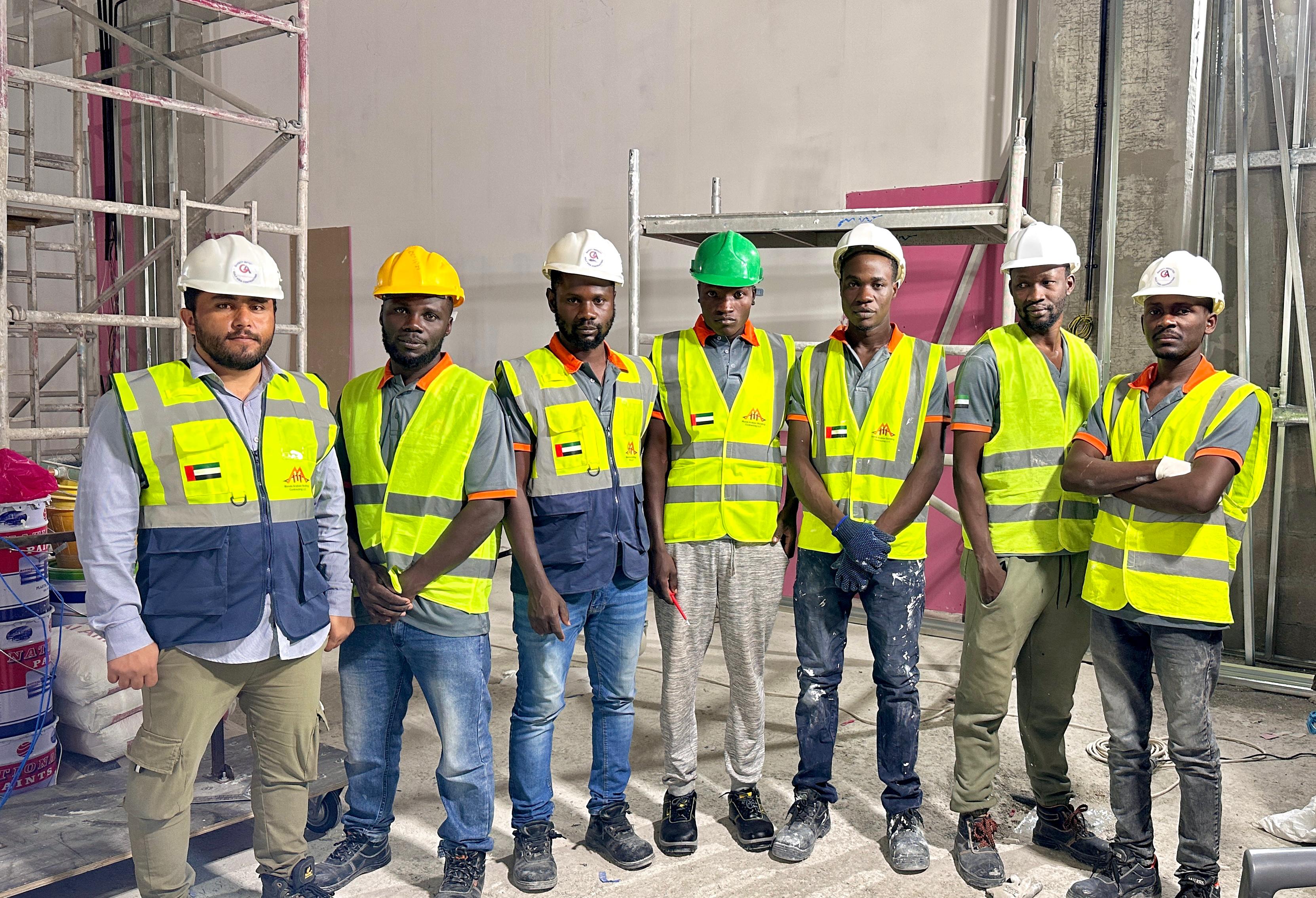 A team of seven construction workers and supervisors, wearing safety gear including hard hats and high-visibility vests