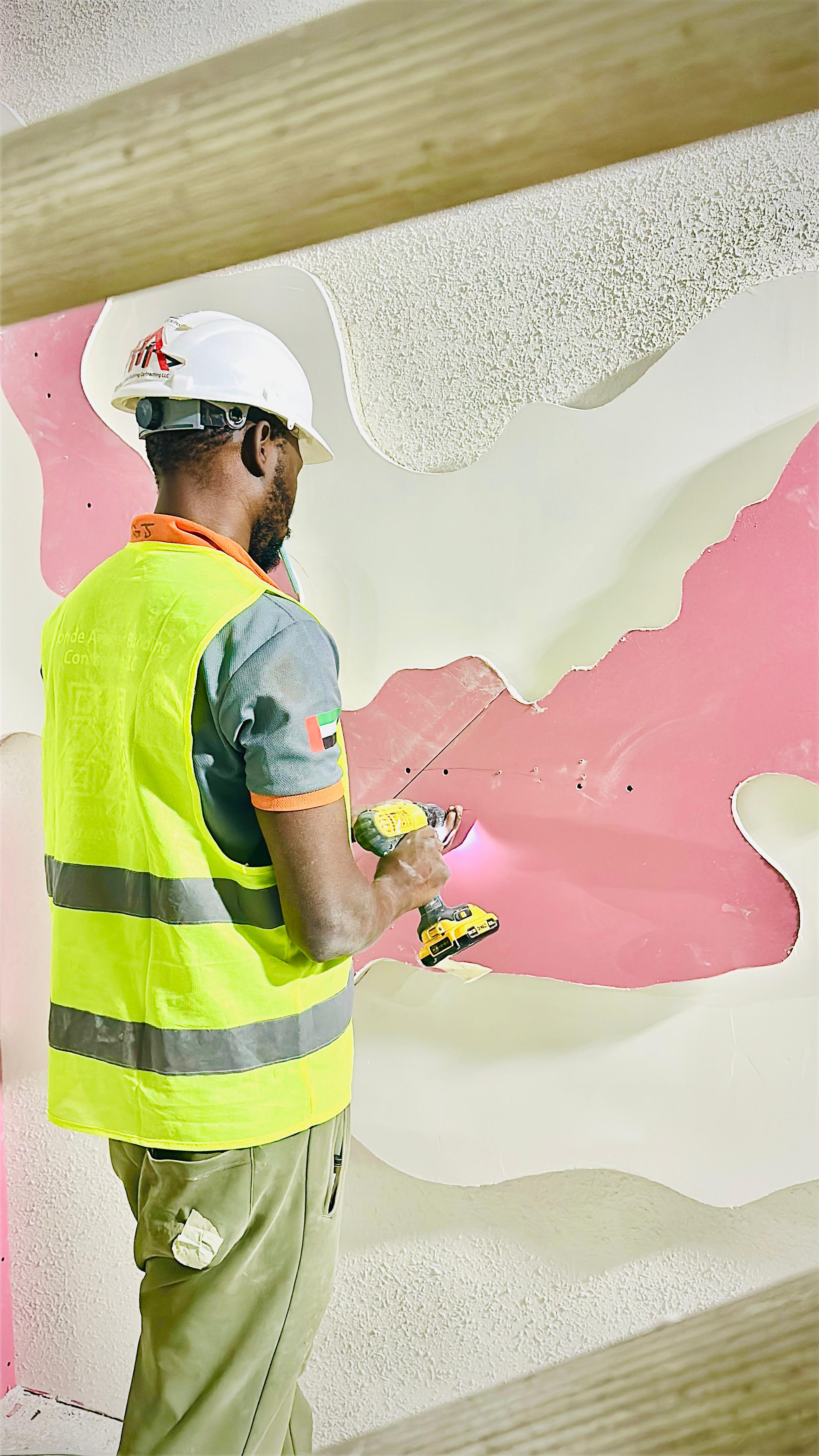 A construction worker in a hard hat and safety vest uses a power drill to install wall panels