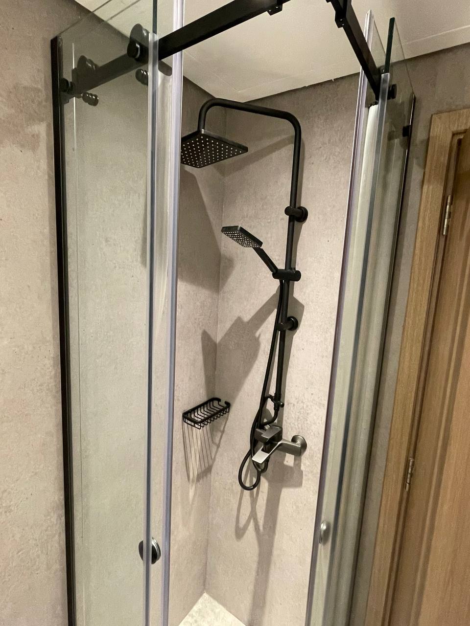 A modern and minimalist bathroom features a walk-in shower with a black-framed glass enclosure and rain shower head