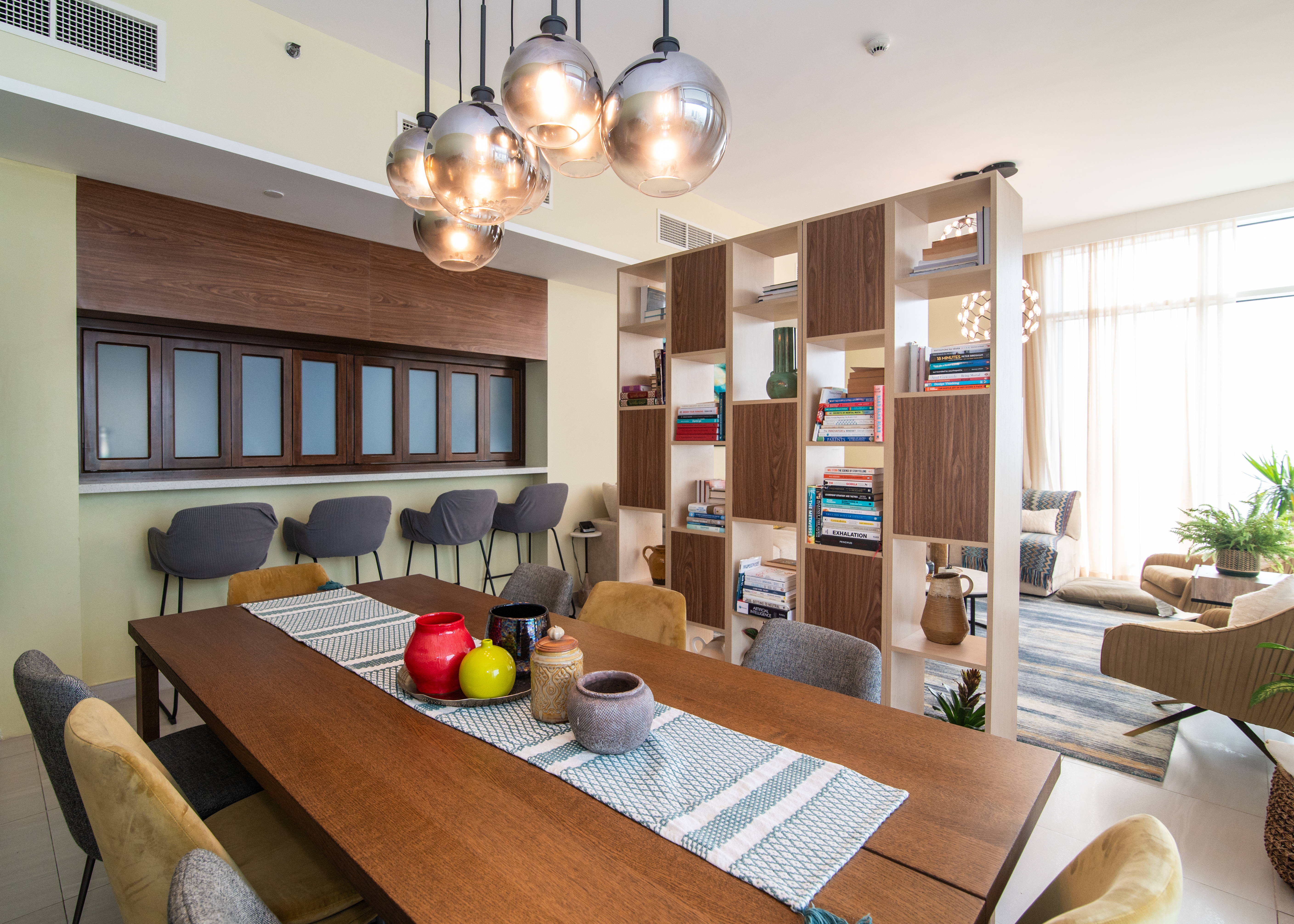 Open-plan dining with walnut table, pendant cluster and bookshelf divider