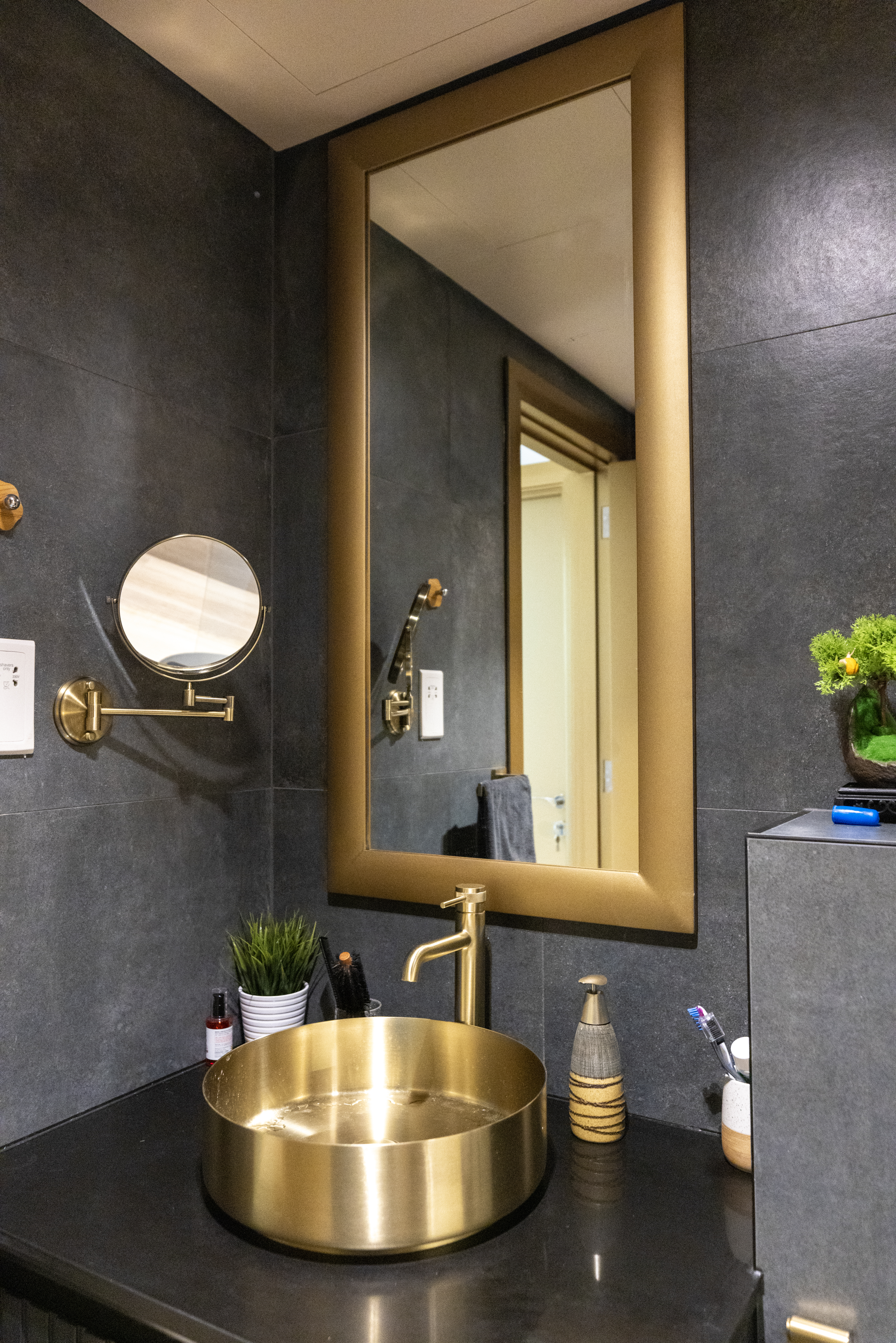 Dark stone bathroom with brass vessel sink and framed mirror