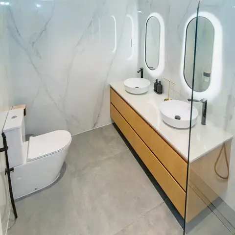 A bright and modern bathroom featuring a floating light wood dual vanity with white vessel sinks, black matte faucets, and backlit oval mirr