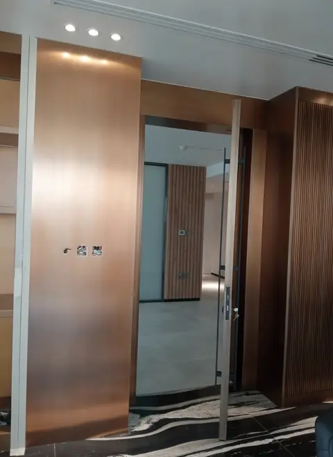 A modern interior hallway features a striking bronze-finished pivot door, flanked by rich wood — APEX STEEL WORKS L.L.C