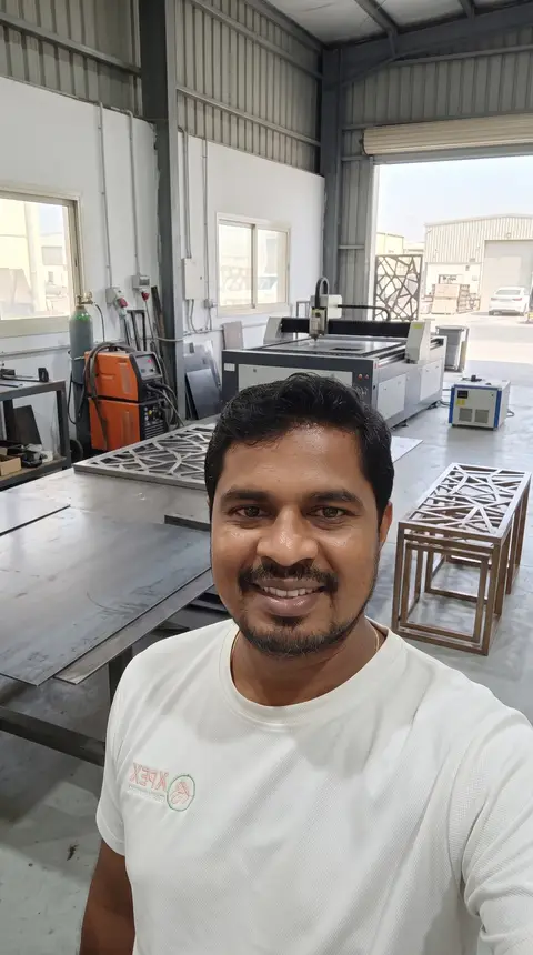 A smiling man takes a selfie in a bright industrial workshop, showcasing a large laser cutting — APEX STEEL WORKS L.L.C