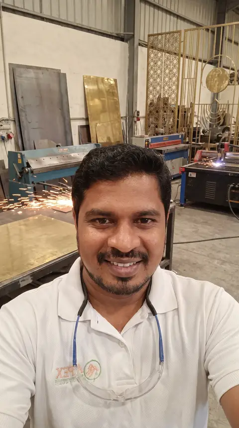 A smiling craftsman in a white polo shirt and safety glasses looks directly at the camera, standing — APEX STEEL WORKS L.L.C