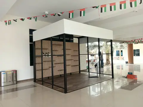 A bright modular display kiosk with black metal grid framing, pegboard shelving, and wood-look — APEX STEEL WORKS L.L.C, UAE