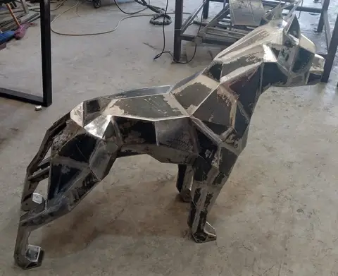 A striking geometric metal sculpture of a dog, showcasing its raw, polygonal form and visible weld — APEX STEEL WORKS L.L.C