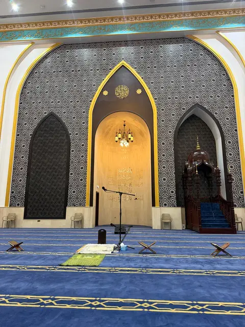 An ornate mihrab with golden calligraphy, a multi-tiered chandelier, and intricate geometric wall patterns — Malak Afzal