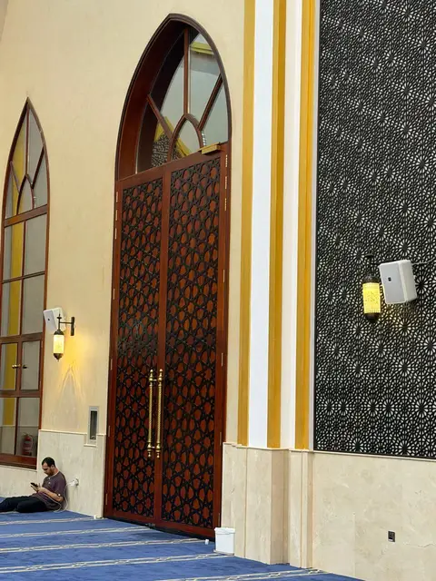 Ornate dark wood double doors with intricate geometric patterns and tall arched windows are set against cream — Malak Afzal