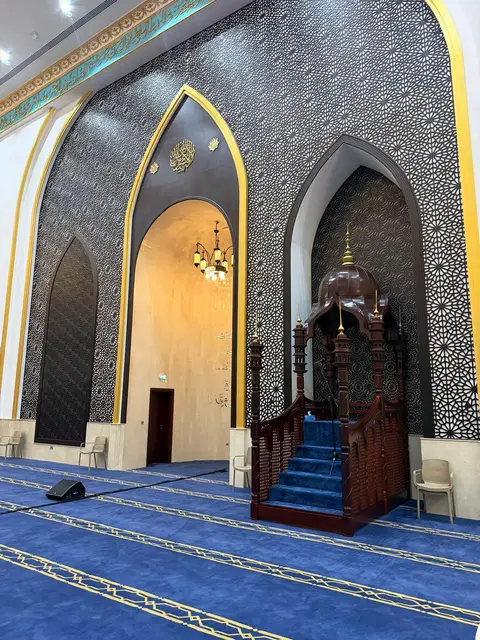 Intricate black and gold geometric patterns adorn arched walls, a richly carved dark wood minbar, and a — Malak Afzal