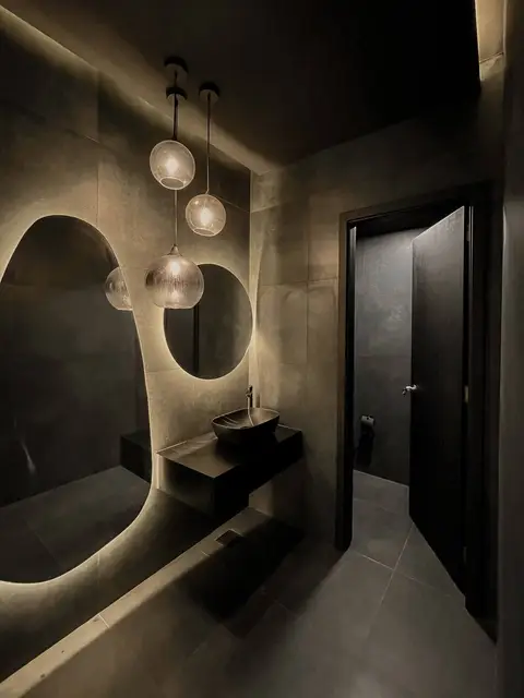 A dark floating vanity with a black vessel sink, backlit mirror, and globe — CRAFTY CLARE DECORATION DESIGN L.L.C, Dubai