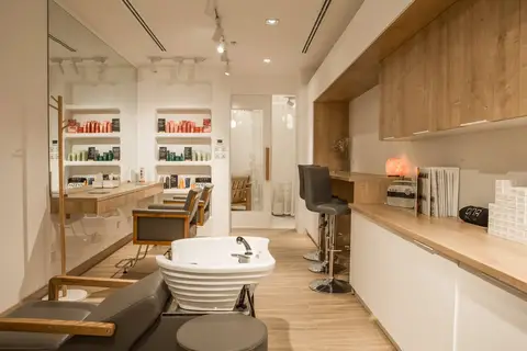 A modern hair salon interior features light wood accents, white cabinetry — CRAFTY CLARE DECORATION DESIGN L.L.C, Dubai