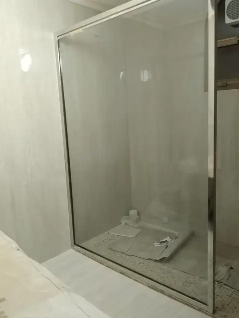 A wide shot captures a modern bathroom shower enclosure under construction, featuring a clear glass partition with a sle