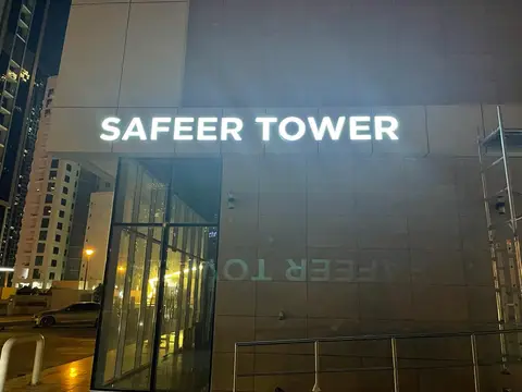 Illuminated 'SAFEER TOWER' signage above a glass entrance is — MINGASH ENGRAVING & ORNAMENTATION WORKS EST., SAFEER TOWER