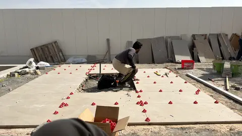 A construction worker is diligently installing large format outdoor tiles on a prepared sub-base, utilizing red leveling