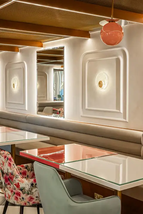 Plush booth seating, glass-topped tables, and floral chairs are set against decorative white wall panels — Muhammed  Gani