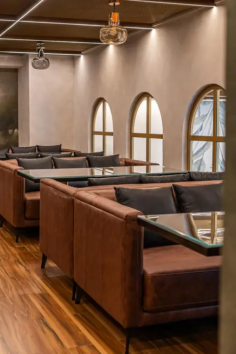 Brown leather booth seating and glass-top tables are set against light beige walls with arched windows and — Muhammed  Gani