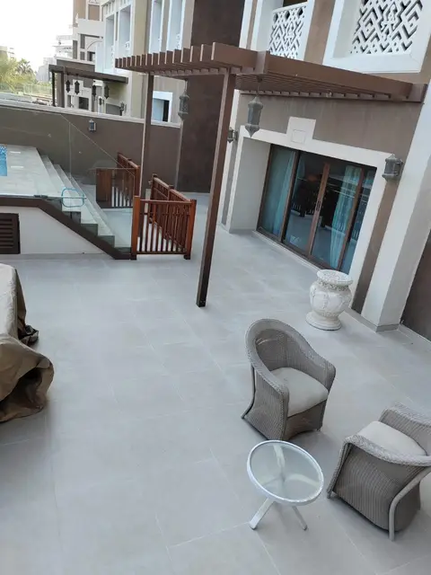A spacious outdoor patio with light grey tiles, a modern wooden pergola, and comfortable wicker seating — A&B Design & Build