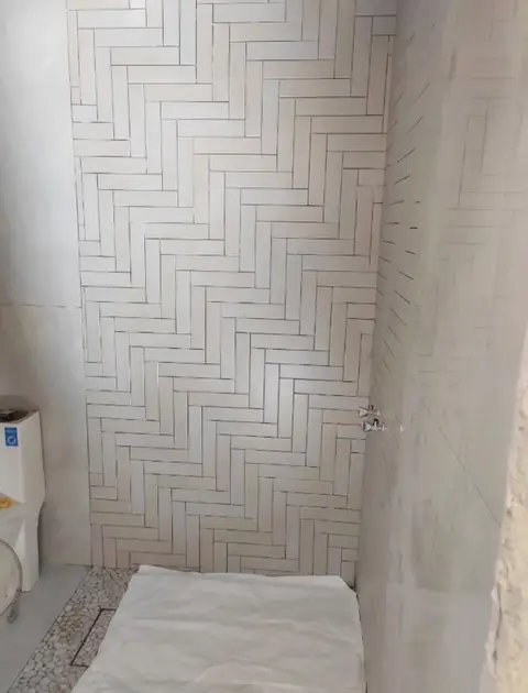 Modern bathroom renovation underway with white herringbone tile accent wall, pebble flooring, and — A&B Design & Build