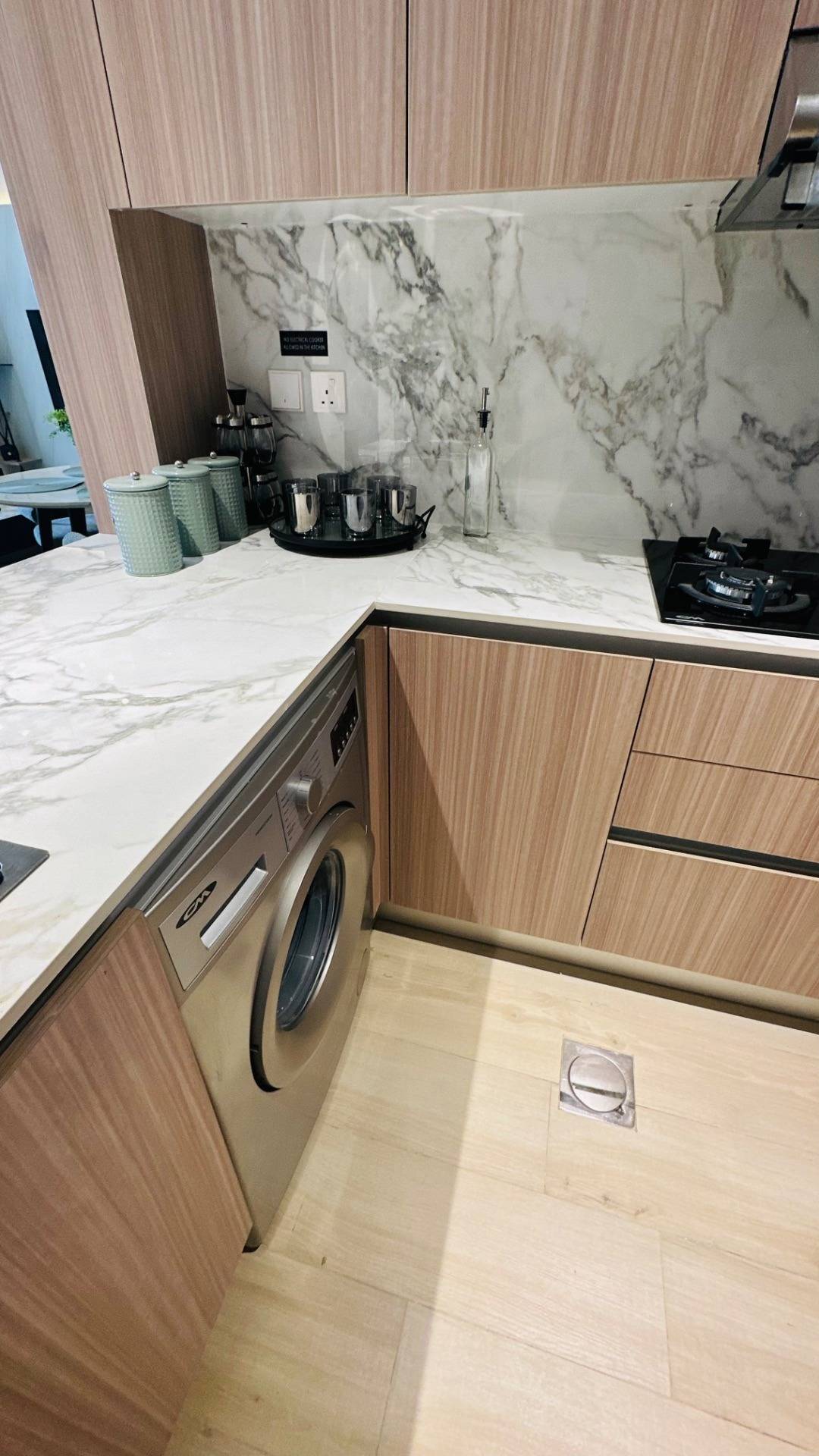 Compact kitchen with light wood cabinetry, white marble-look worktops and backsplash, an integrated washing machine and a gas hob, produced by our joinery and stone team
