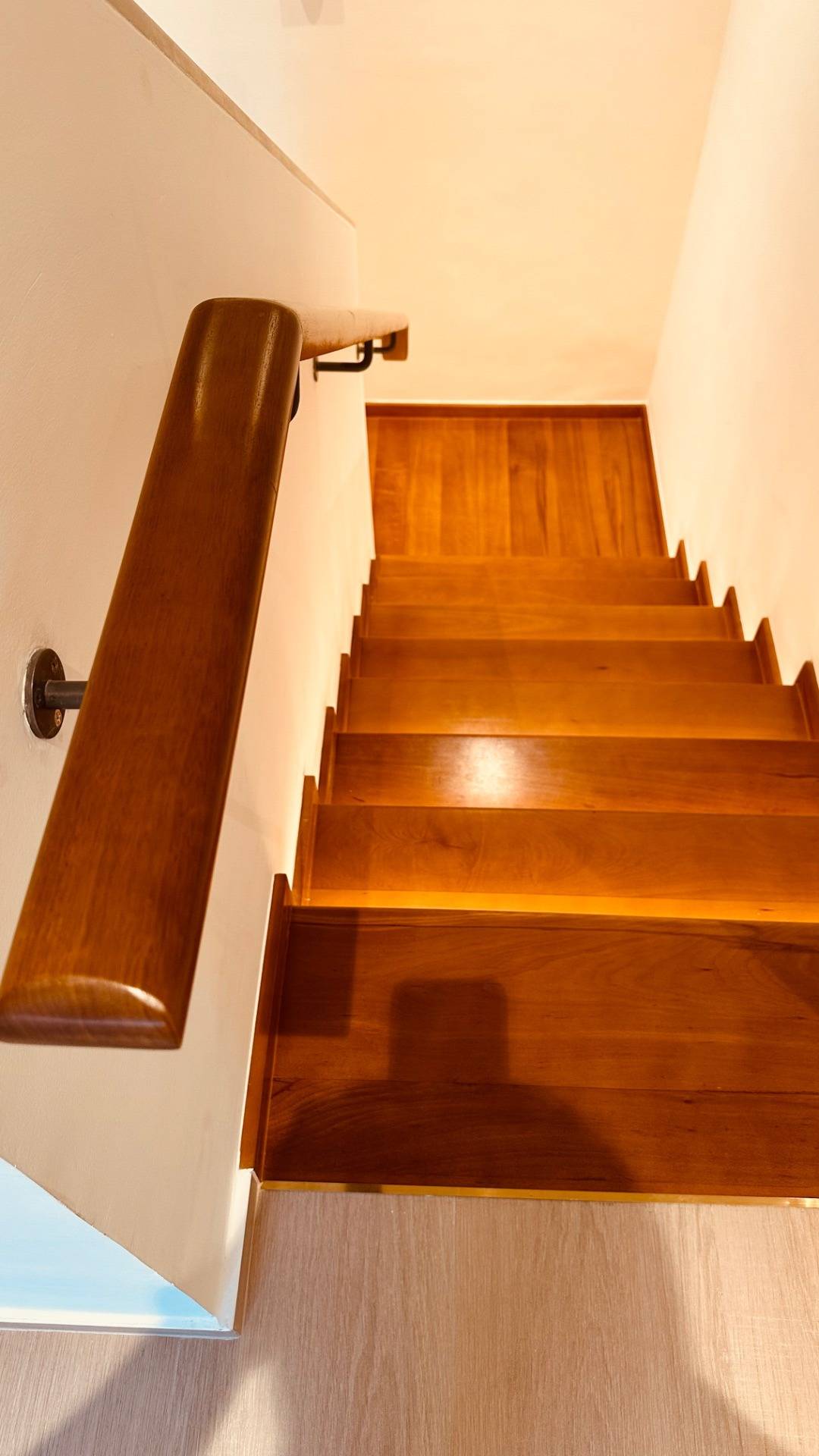 Wooden staircase with a sleek timber handrail lit by warm lighting that highlights the grain of the wood.