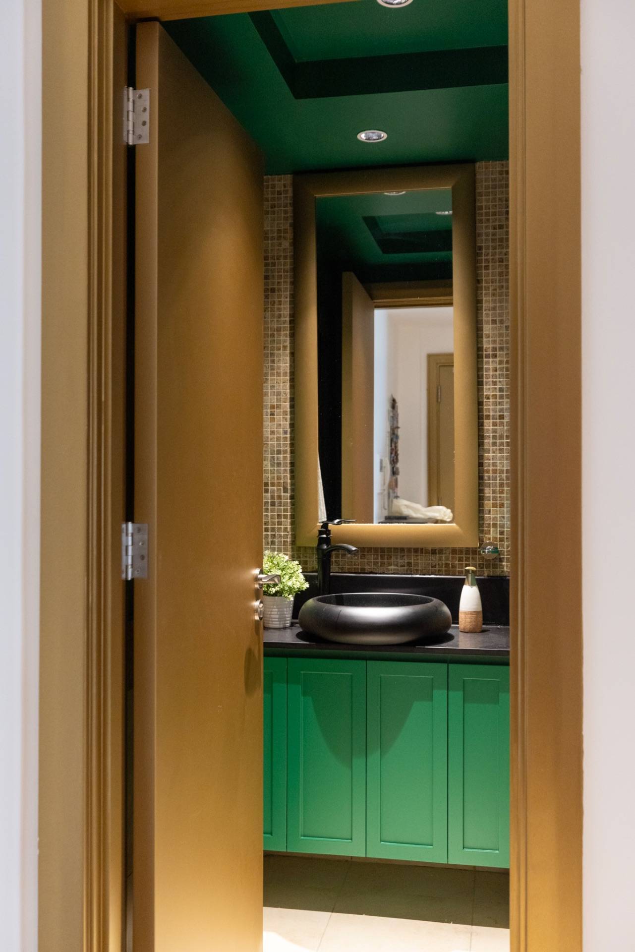 Modern powder room in Abu Dhabi with an emerald green ceiling and vanity, black vessel sink and gold-framed mirror over mosaic tiles