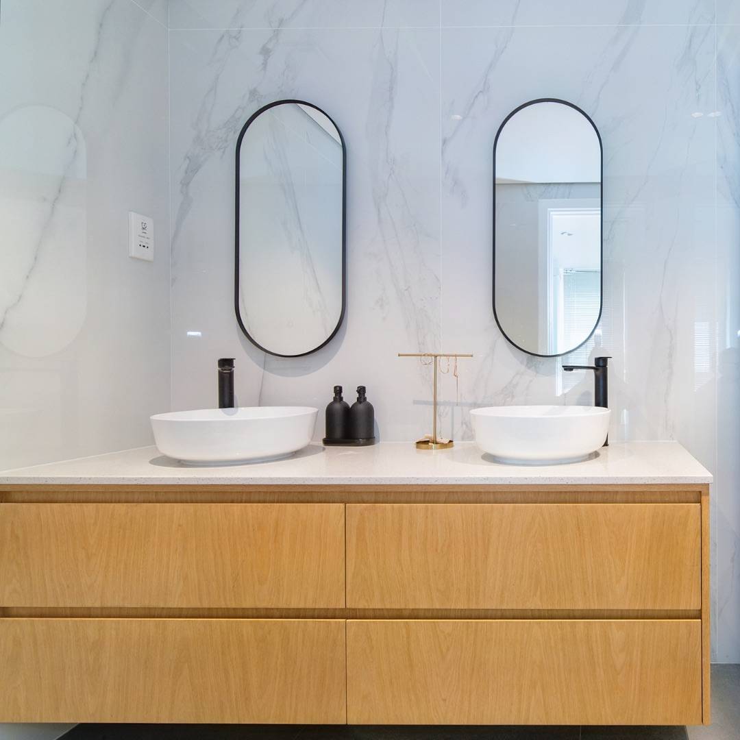 Light wood double vanity with white vessel sinks and matte black faucets against a white marble-look tiled wall