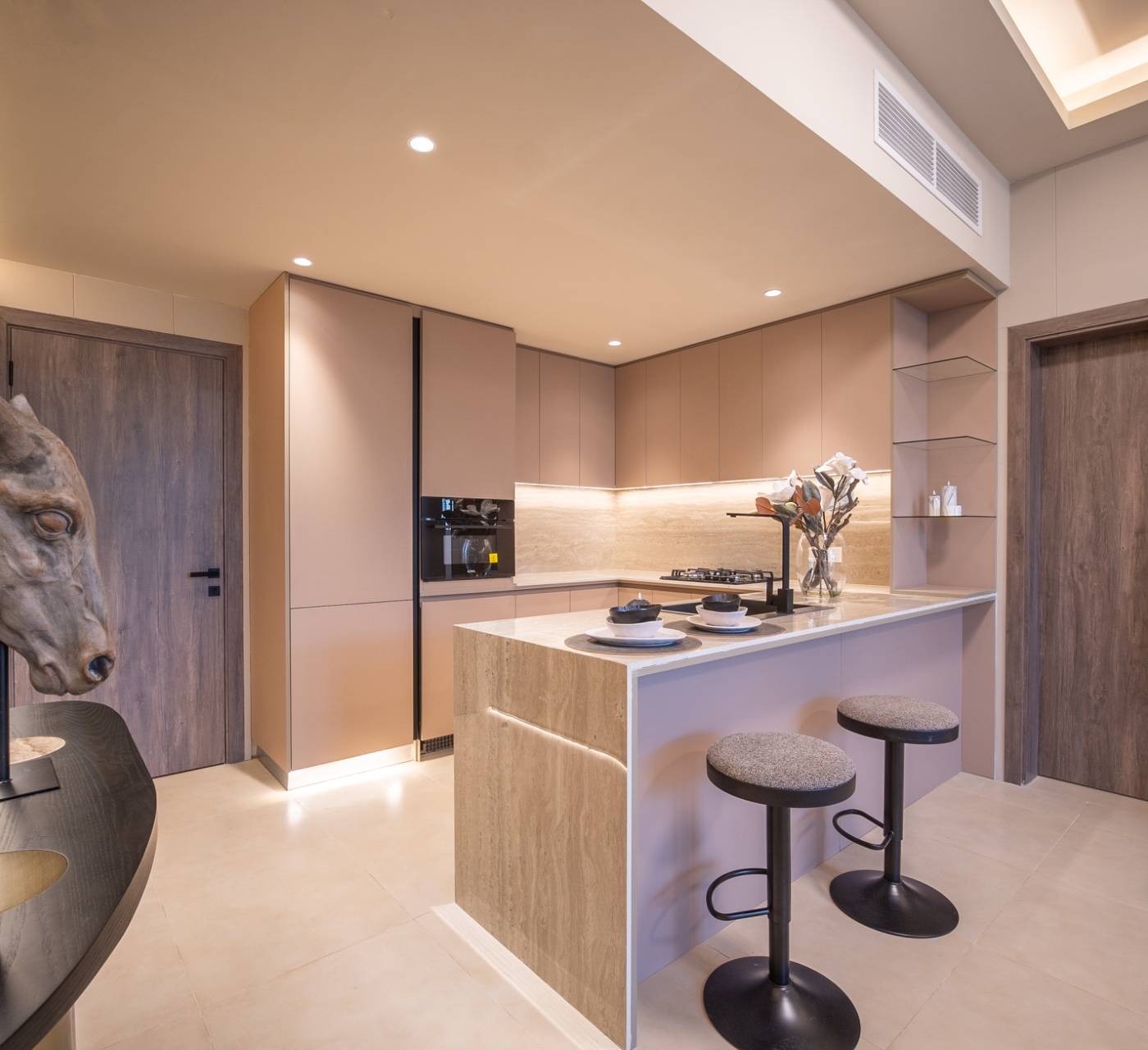 Modern kitchen with warm neutral tones, central island with bar seating, integrated appliances, strip lighting and horse head sculpture — villa remodeling Dubai detail shot.
