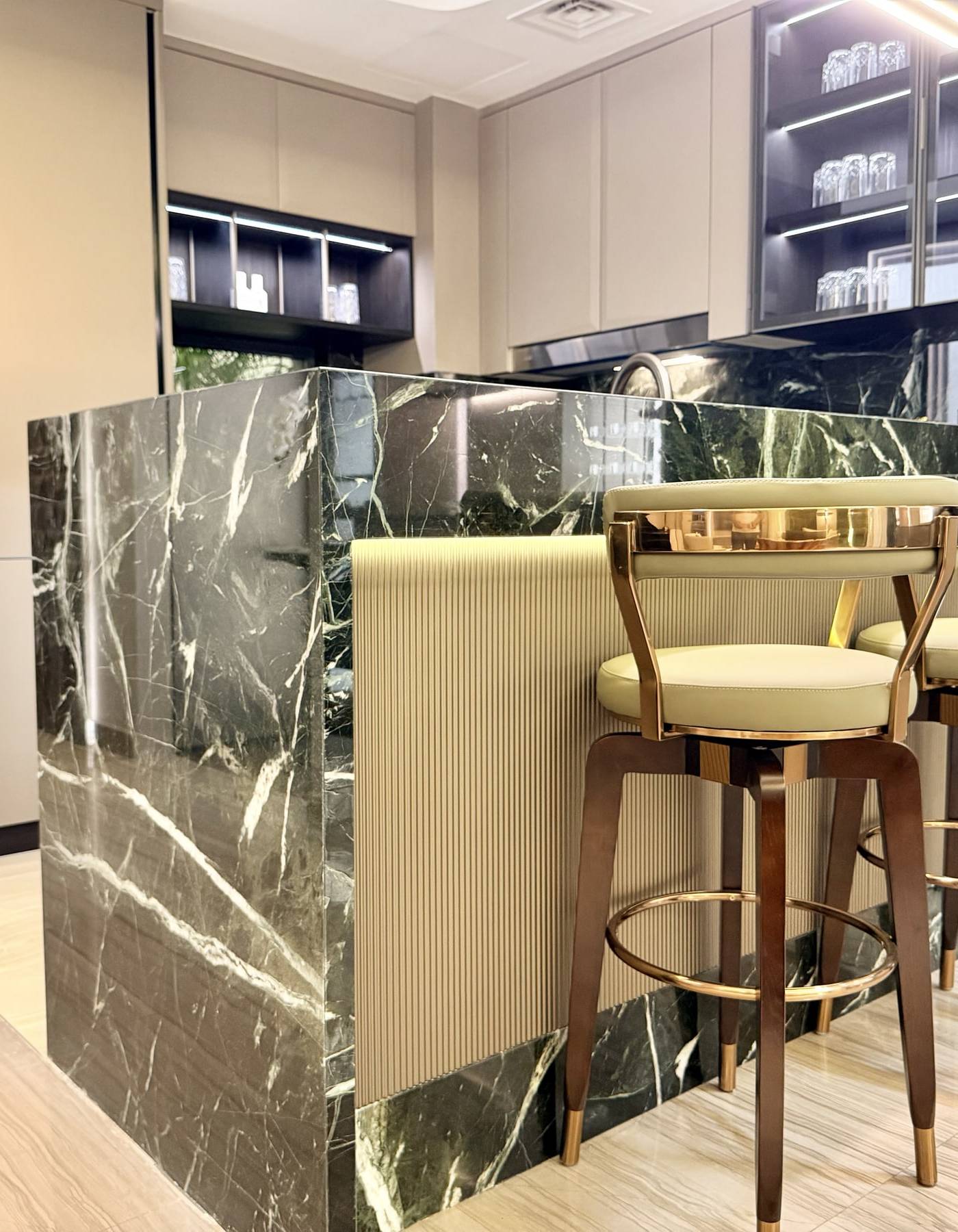 Dark green marble island with gold accented bar stools, integrated lighting and fluted panelling in a Dubai kitchen, showing the finish level MODENZO brings to kitchens and fitted wardrobes Dubai clients commission.