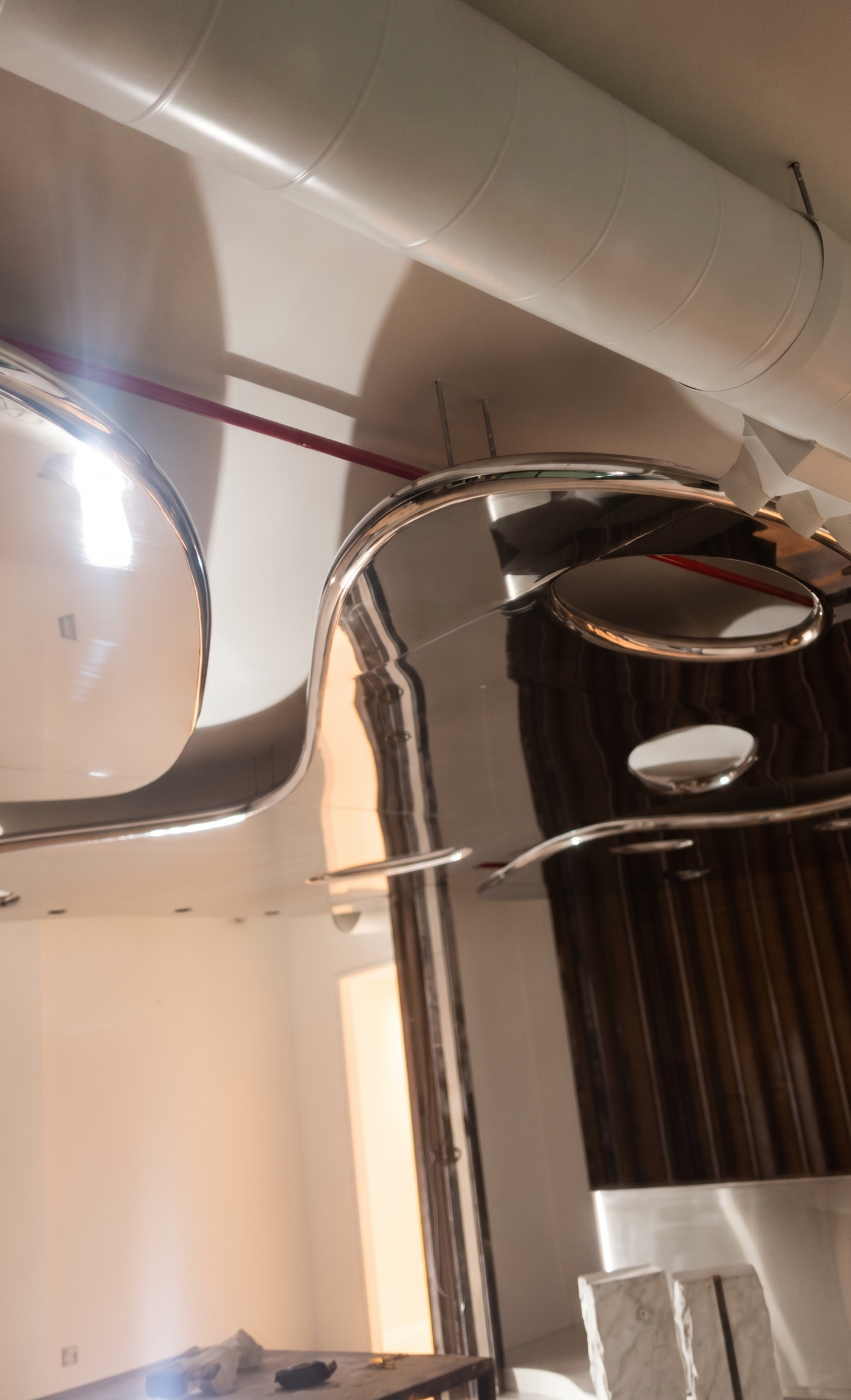 High angle view of reflective sculptural chrome ceiling elements in a modern interior with white walls, industrial white ductwork and red conduit