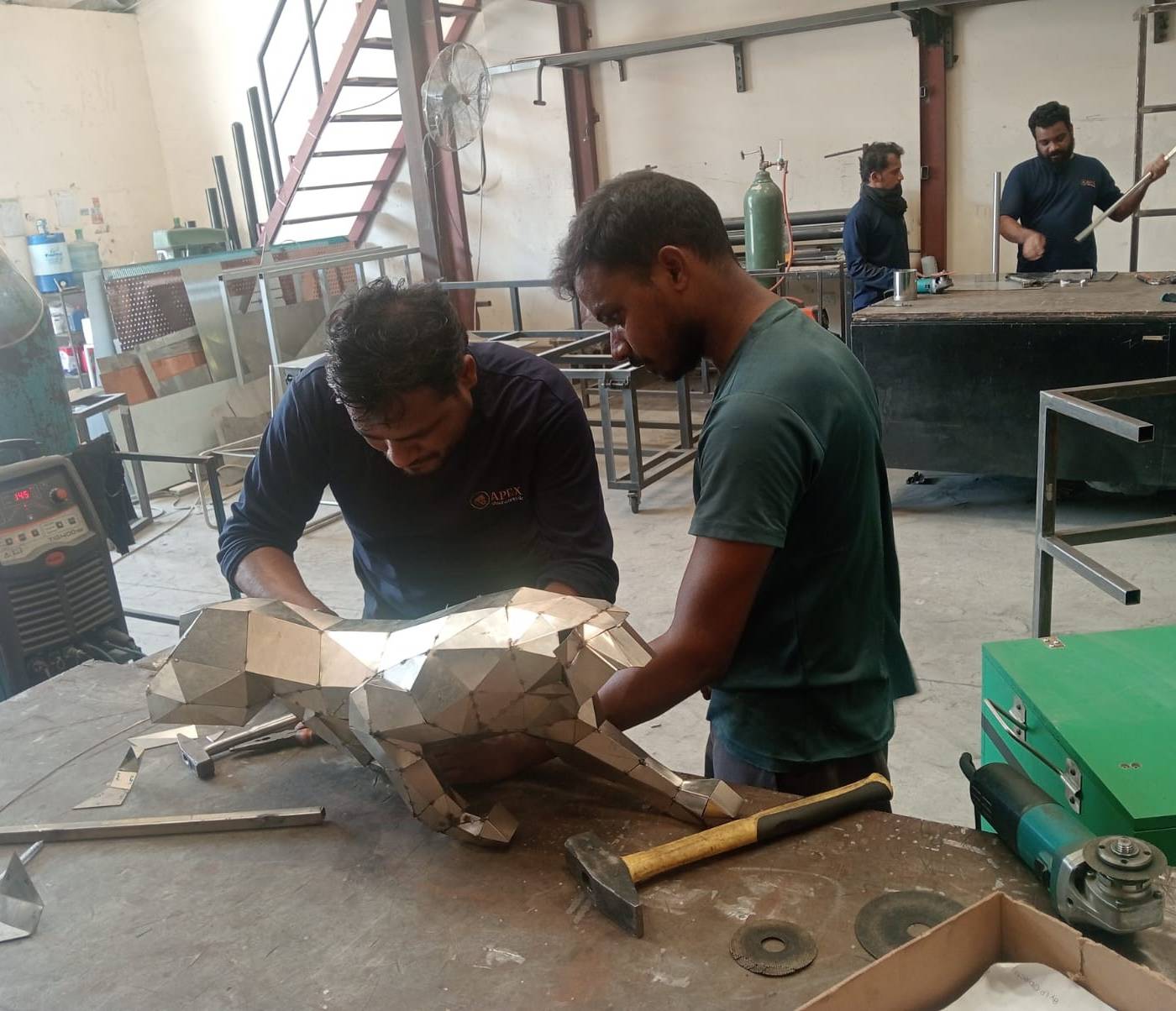 Fabricators assembling a geometric metal animal sculpture in a Dubai steel workshop surrounded by tools and fabrication equipment