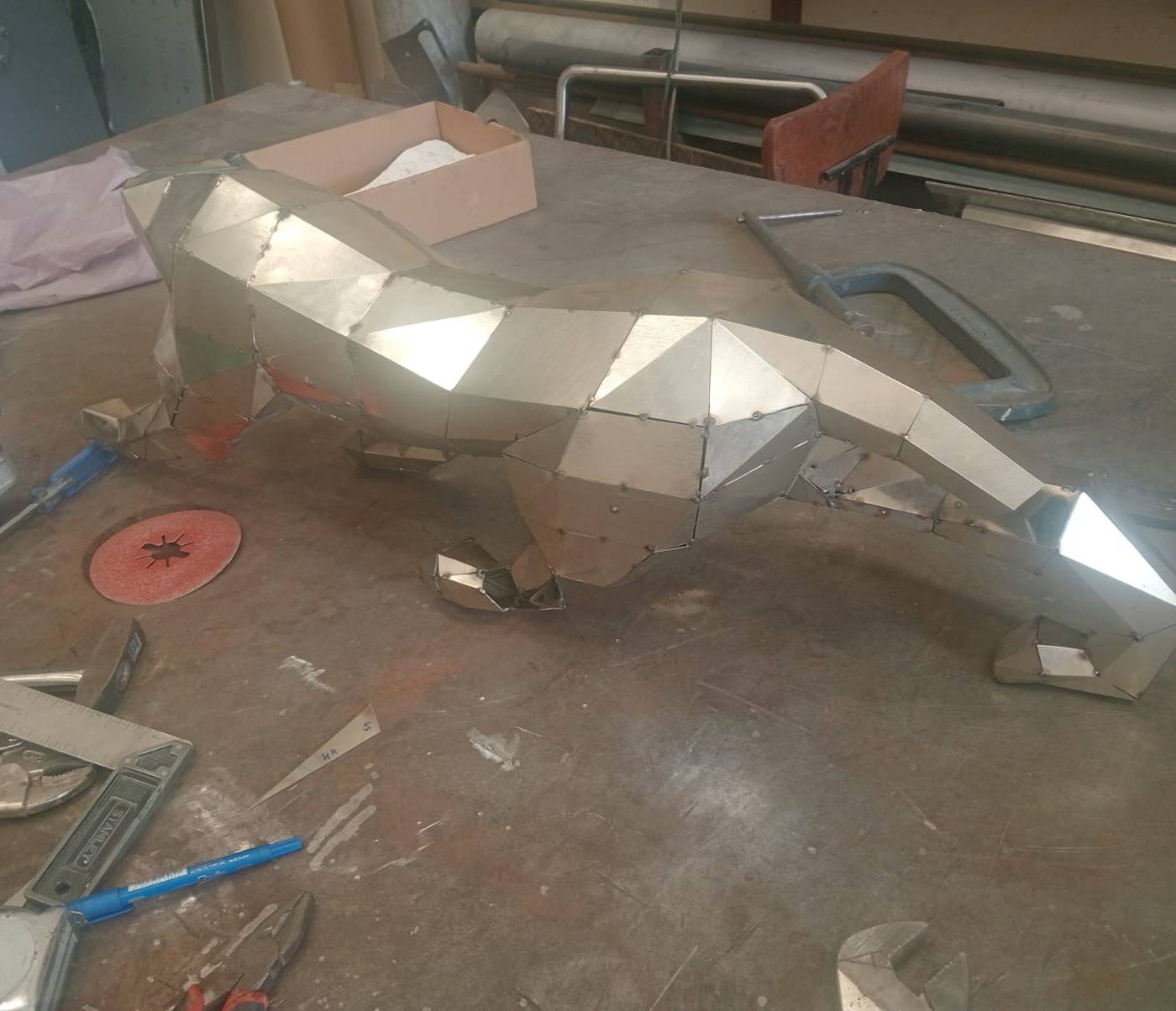 Geometric metal fox sculpture assembled from polished panels on a workshop table at APEX Steel Works, showing structural <a href=