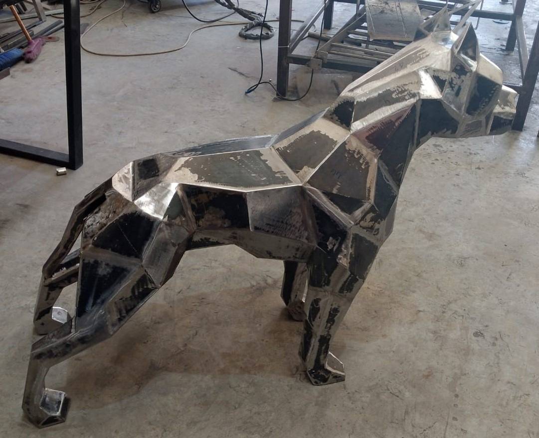 Geometric metal dog sculpture with raw polygonal form and visible weld marks on an Abu Dhabi steel fabrication workshop floor