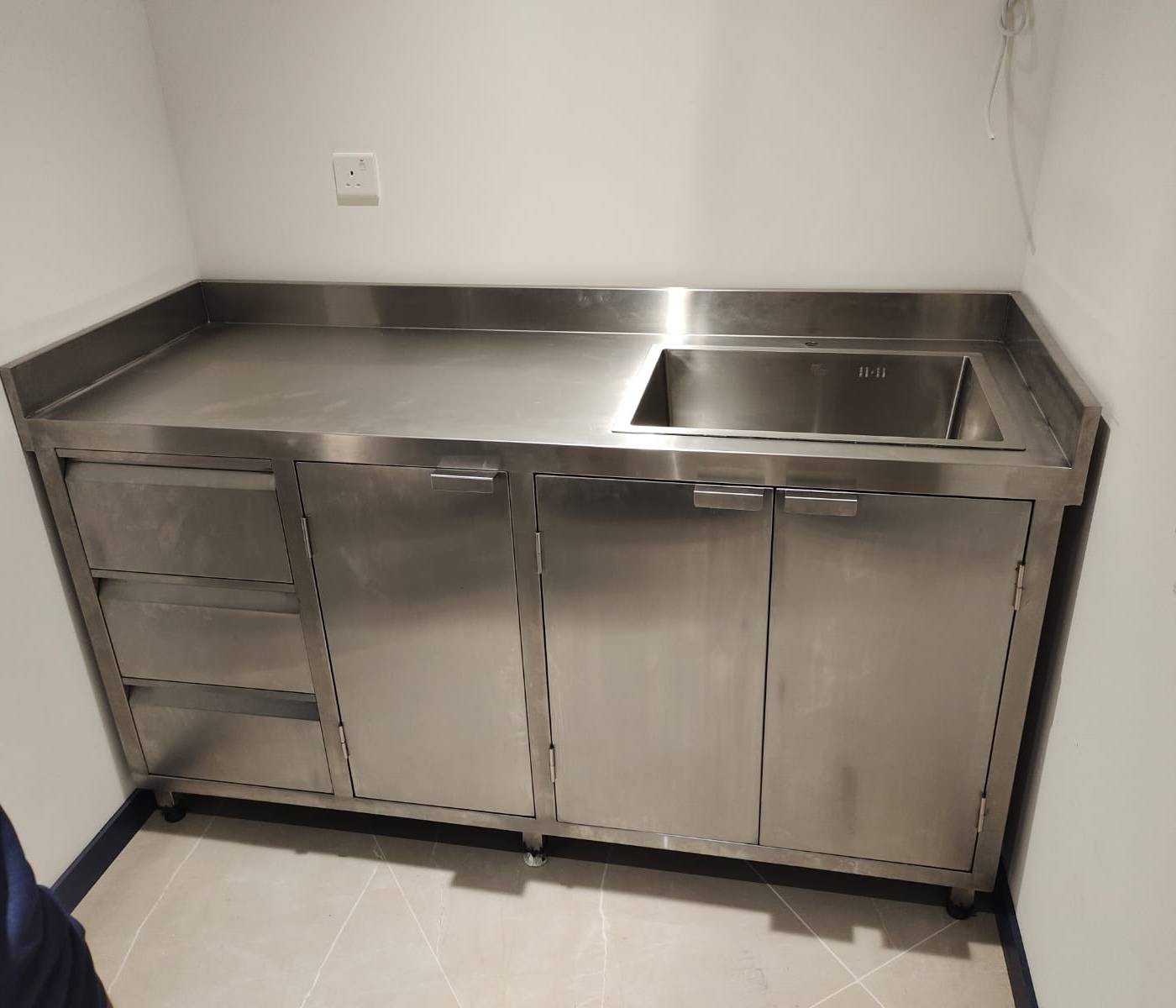 Stainless steel utility counter with an integrated sink, three drawers and two double-door cabinets, fabricated by our workshop as part of structural <a href=