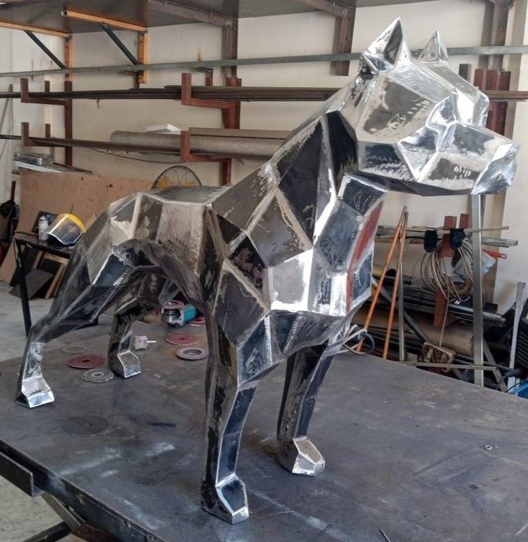 Geometric metal pitbull sculpture in raw unfinished stages on a fabrication workbench at APEX Steel Works, UAE