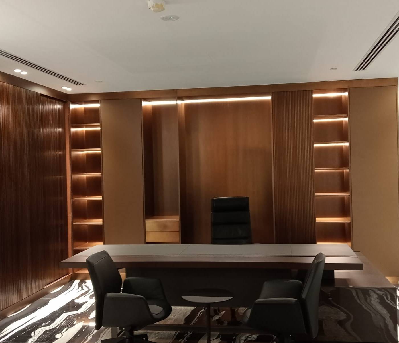 Executive office steel fabrication with dark wood paneling, integrated LED shelving, grey desk and marble flooring