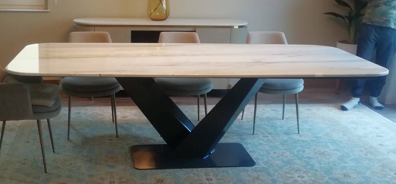 White marble dining table on a black V-shaped metal base with velvet chairs in a contemporary UAE dining space