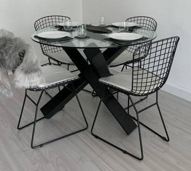 Modern dining area with round glass top table on a black X shaped steel frame in Al Ain