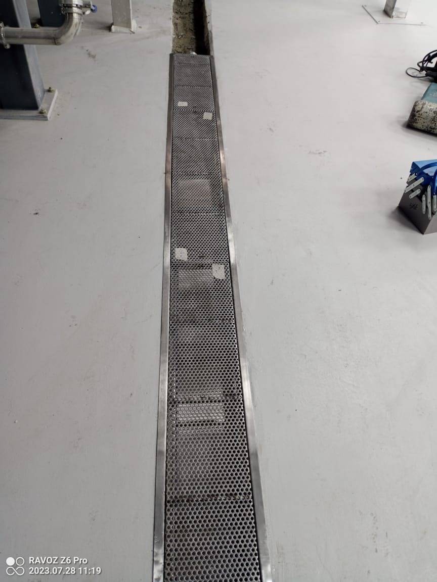 A perforated stainless steel trench drain set into a light grey concrete floor during an APEX steel fabrication project