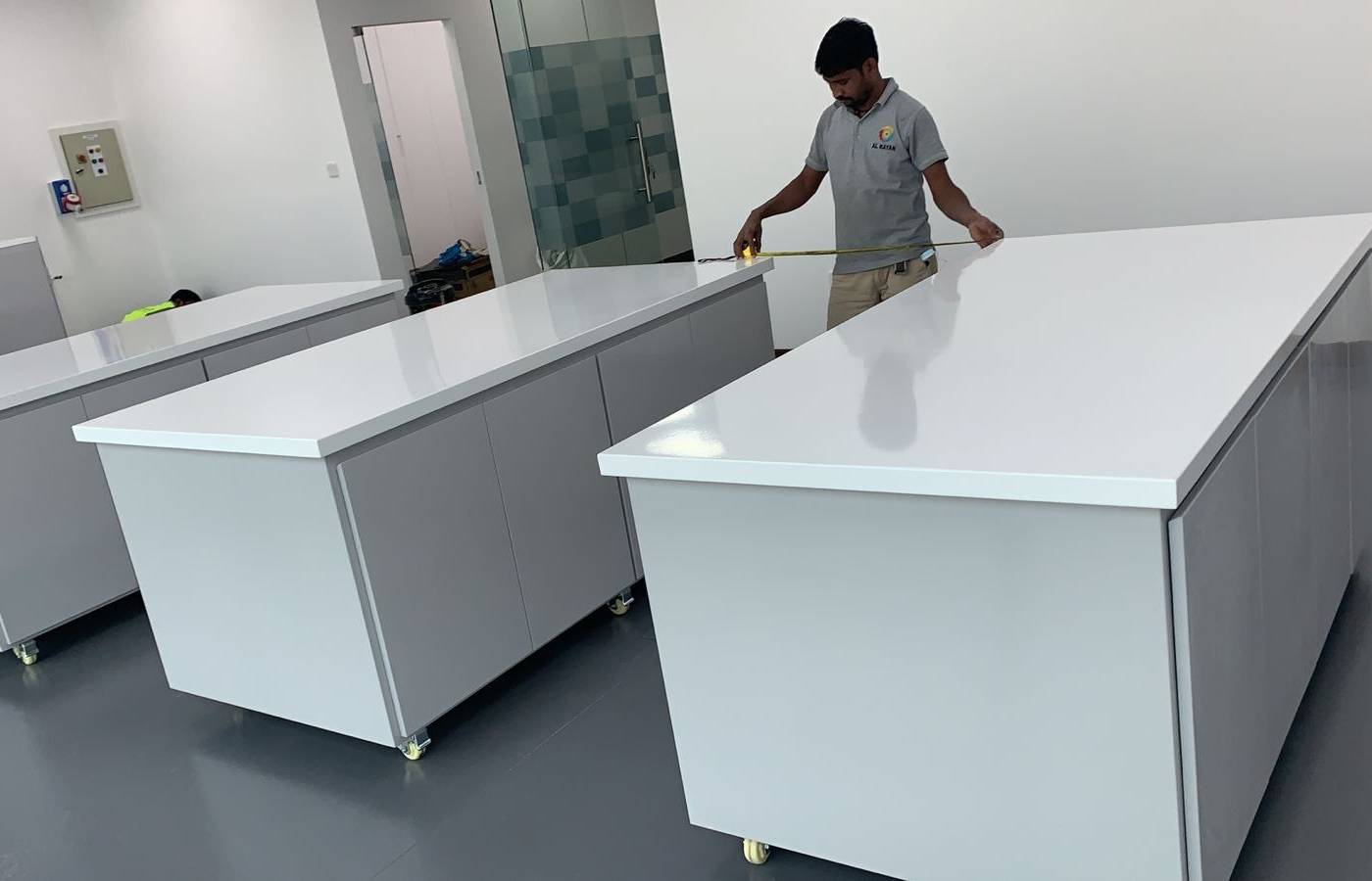 Worker measuring a white countertop on a light grey mobile cabinet during a <a href=