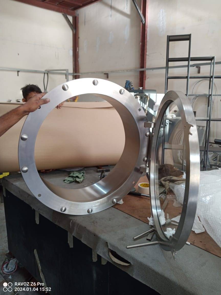 A stainless steel porthole access hatch with clear glass viewport being assembled in APEX Steel Works L.L.C Dubai workshop