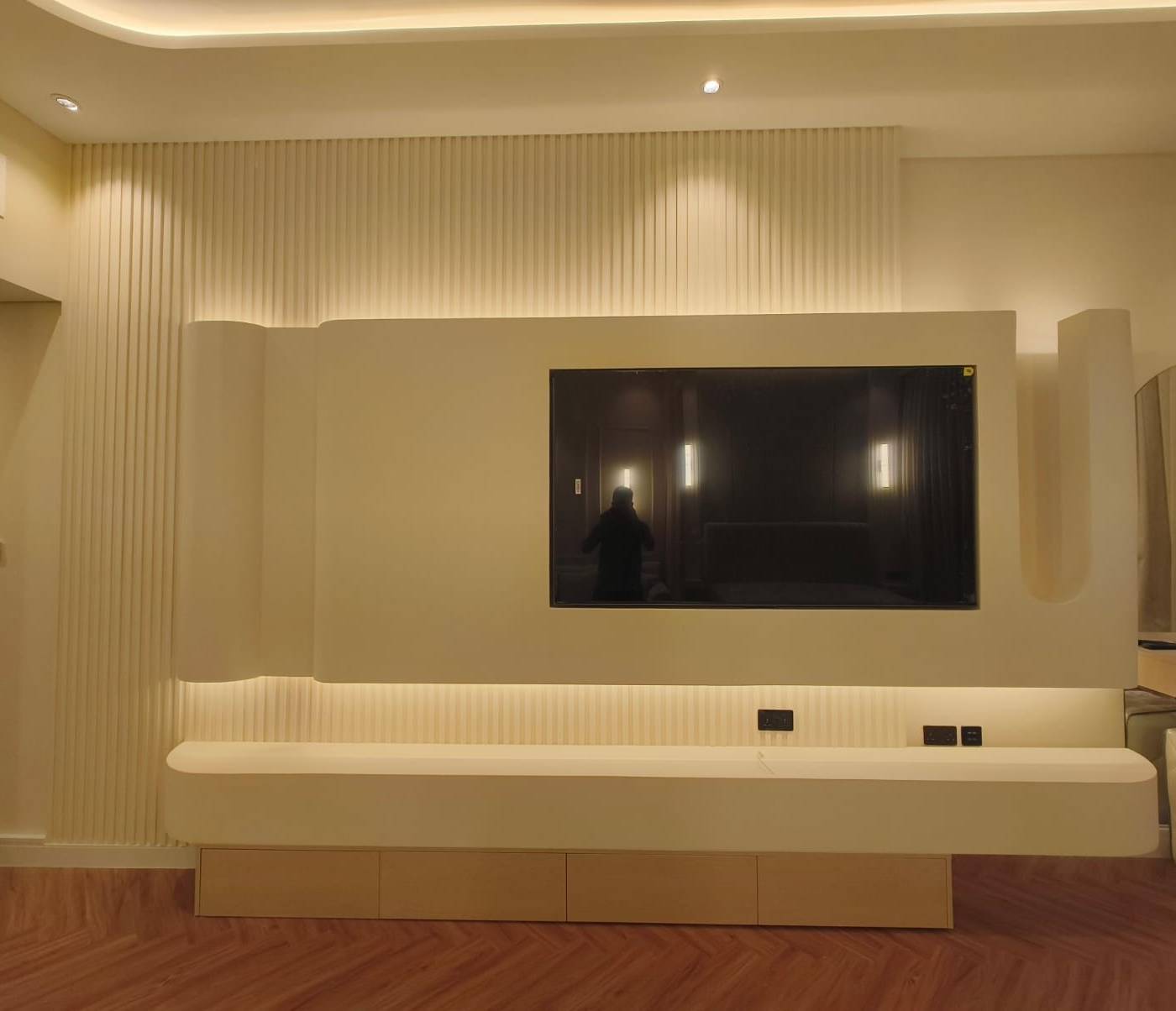 Modern Dubai living room with a custom cream entertainment wall, mounted TV, floating console, warm LED strip lighting and a fluted panel accent over light wood flooring