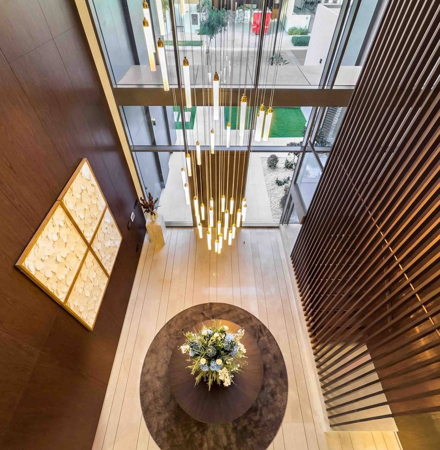 High angle view of a modern lobby renovation in Dubai with a multi tiered chandelier, circular table with blue and white floral arrangement and rich wood paneling