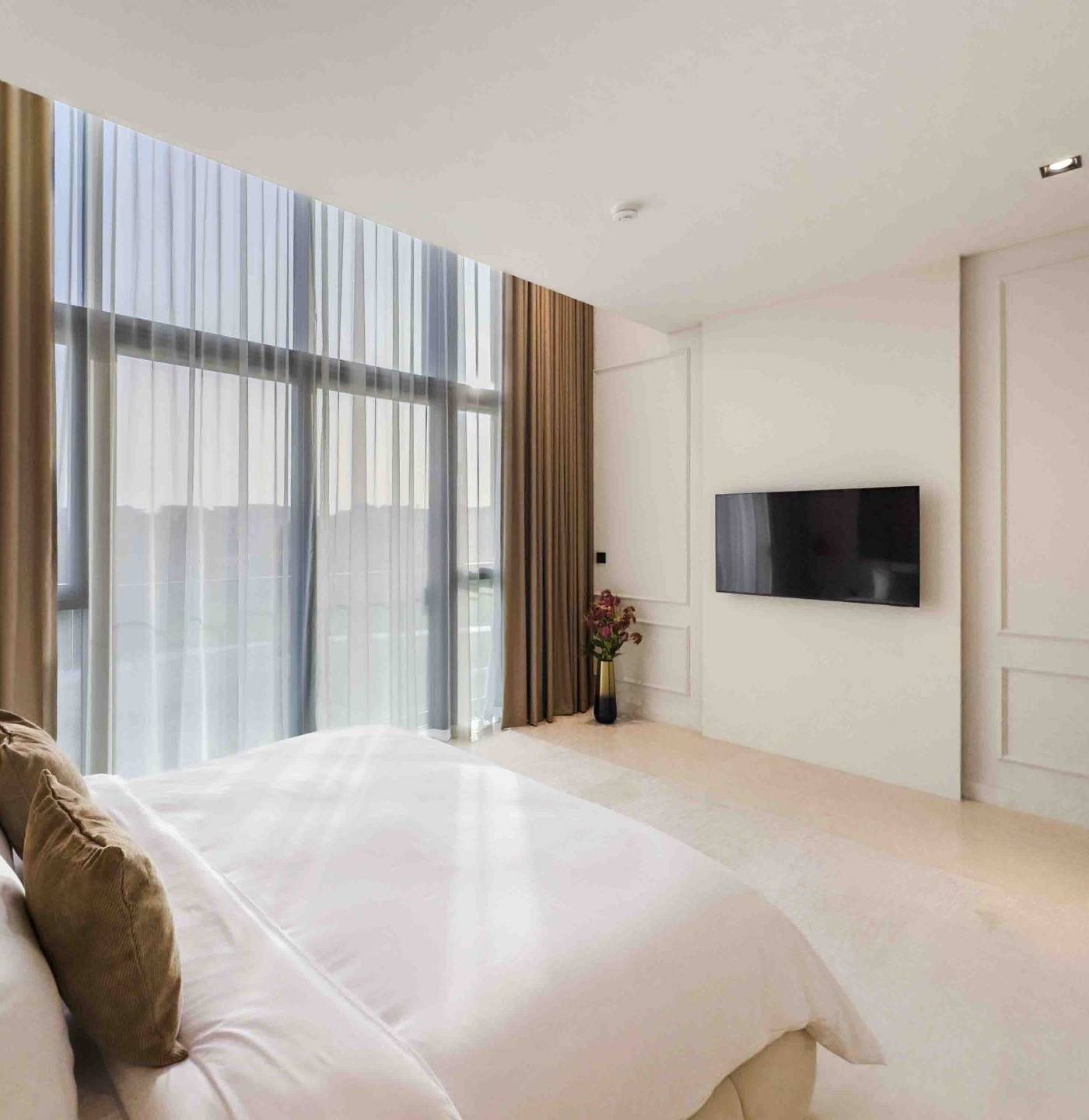 Bedroom with floor to ceiling windows, sheer and blackout curtains and a plush white bed, cooled by a serviced AC unit in Dubai